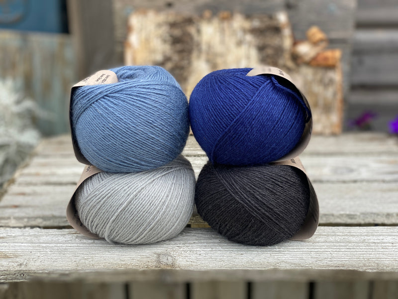 Four balls of yarn. Colours are pale blue, blue, dark blue and black