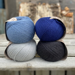 Four balls of yarn. Colours are pale blue, blue, dark blue and black
