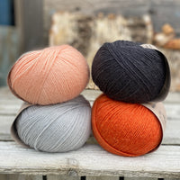 Four balls of yarn. Colours are pale blue, peach, orange and dark grey