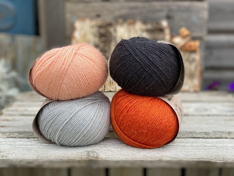 Four balls of yarn. Colours are pale blue, peach, orange and dark grey