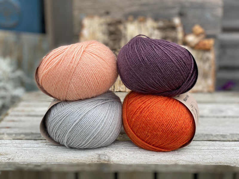 Four balls of yarn. Colours are pale blue, peach, orange and dark purple