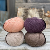 Four balls of yarn. Colours are beige, brown, peach and dark purple