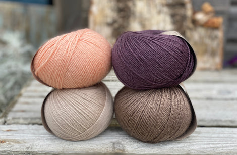 Four balls of yarn. Colours are beige, brown, peach and dark purple
