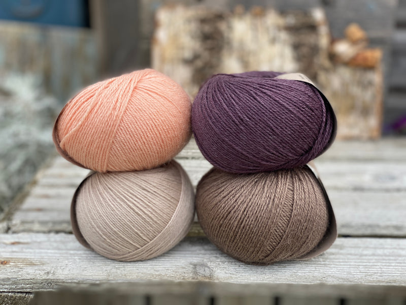 Four balls of yarn. Colours are beige, brown, peach and dark purple