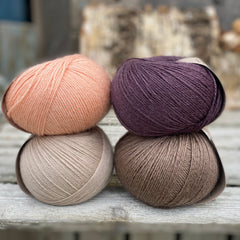 Four balls of yarn. Colours are beige, brown, peach and dark purple