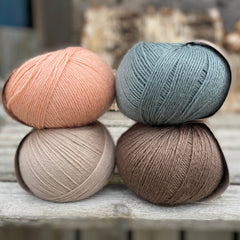 Four balls of yarn. Colours are beige, peachy orange, teal and brown