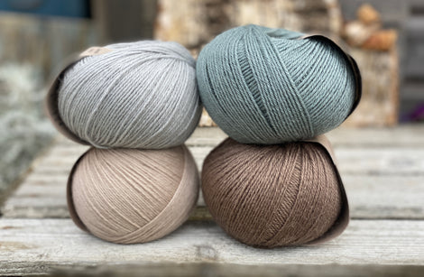 Four balls of yarn. Colours are beige, brown, teal and pale blue