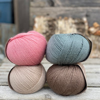 Four balls of yarn. Colours are beige, pink, teal and brown