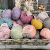 A wicker basket containing seventeen balls of Milburn DK in many colours