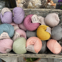A wicker basket containing seventeen balls of Milburn DK in many colours