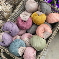 A wicker basket containing seventeen balls of Milburn DK in many colours