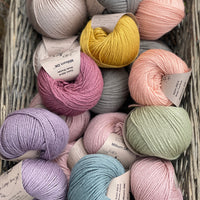 A wicker basket containing seventeen balls of Milburn DK in many colours