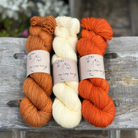Three skeins of yarn. From left to right: an orangey brown skein, a creamy yellow skein and a dark orange skein