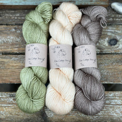 Three skeins of yarn. From left to right: a green skein, a cream skein and a brown skein