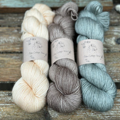 Three skeins of yarn. From left to right: a cream skein, a brown skein and a greeny-grey skein