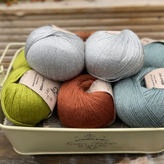 Eight balls of yarn in four pairs. From left to right the colourways are green, red-brown and blue-green with light blue sat on top