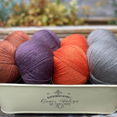 Eight balls of yarn in four pairs. From left to right the colourways are red-brown, purple, orange and grey