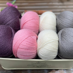 Eight balls of yarn in four pairs. From left to right the colourways are purple, pink, cream and grey