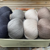 Eight balls of yarn in four pairs. From left to right the colourways are black, grey, beige and brown