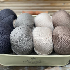 Eight balls of yarn in four pairs. From left to right the colourways are black, grey, beige and brown