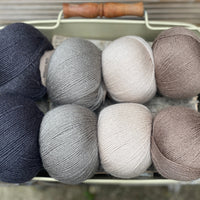 Eight balls of yarn in four pairs. From left to right the colourways are black, grey, beige and brown