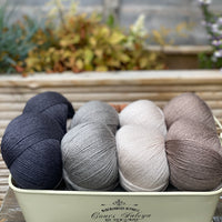 Eight balls of yarn in four pairs. From left to right the colourways are black, grey, beige and brown