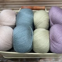 Eight balls of yarn in four pairs. From left to right the colourways are beige, blue-green, pale green, light purple