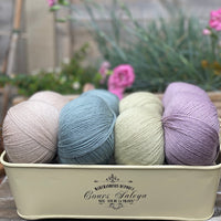 Eight balls of yarn in four pairs. From left to right the colourways are beige, blue-green, pale green, light purple