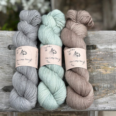 Three skeins of yarn. From left to right: a grey skein, a pale green skein and a brown skein
