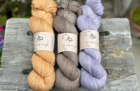 Three skeins of yarn. From left to right: a golden brown skein, a brown skein and a pale purpley blue skein