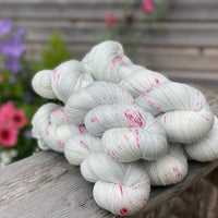 Five skeins of fine silver yarn with bright pink speckles resting on a wooden stool