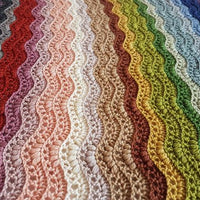 Close up image of a crochet blanket featuring a striped ripple stitch pattern. The blanket uses all twenty colours of Milburn DK. The pattern is Elysium by Sarah Alderson