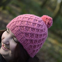Victoria holding a pink hat with a cable lattice pattern and a pink pom pom