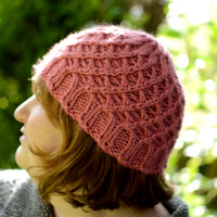 Victoria wearing a bright pink beanie hat with an all over lattice cable stitch pattern