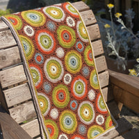 A crocheted rectangular wrap which has an all-over motif of multicoloured circles.