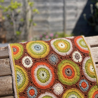 A crocheted rectangular wrap which has an all-over motif of multicoloured circles.