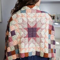 A person with long brown hair wearing a patchwork granny square jacket over blue dungarees