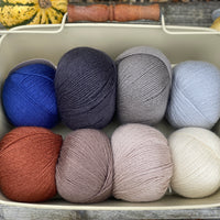 Eight balls of Milburn 4ply in shades of brown and grey with pops of red and blue