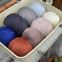 Eight balls of Milburn 4ply in shades of brown and grey with pops of red and blue