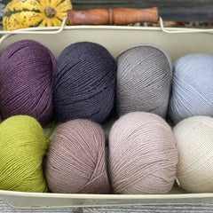 Eight balls of Milburn 4ply in shades of brown and grey with pops of purple and green 