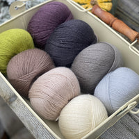 Eight balls of Milburn 4ply in shades of brown and grey with pops of purple and green