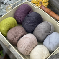 Eight balls of Milburn 4ply in shades of brown and grey with pops of purple and green