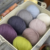 Eight balls of Milburn 4ply in shades of brown and grey with pops of purple and green