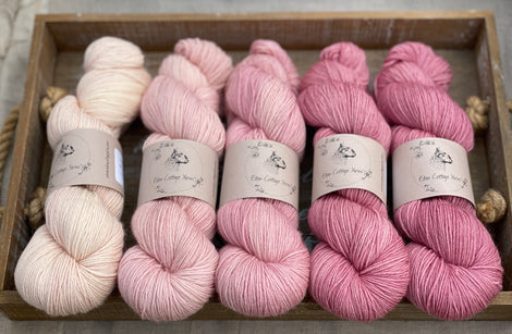 Five skeins of yarn fading from light pink to pink.