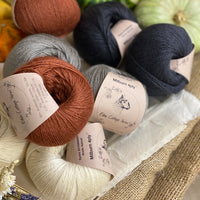 Eight balls of yarn in four colours. The colours are cream, grey and dark grey with a contrast of reddish brown