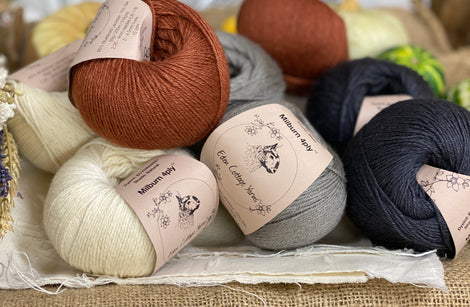Eight balls of yarn in four colours. The colours are cream, grey and dark grey with a contrast of reddish brown