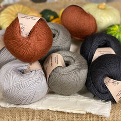 Eight balls of yarn in four colours. The colours are pale grey, mid grey and dark grey with a contrast of reddish brown