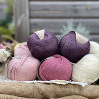 Eight balls of yarn in four colours, two each of natural cream, pale pink, dark pink and dark purple