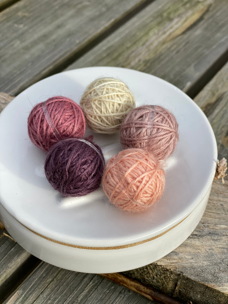 Five small balls of yarn in muted pinks and purple
