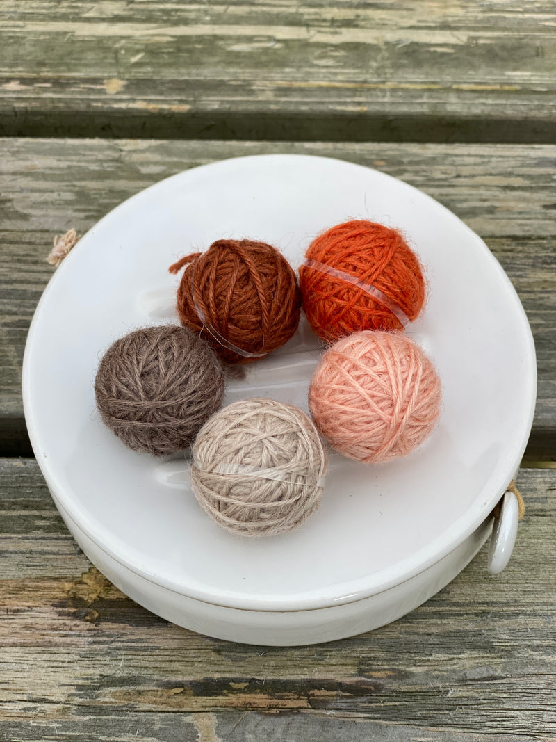 Five small balls of yarn in shades of orange and brown